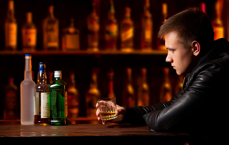 Человек сидит за барным столом, выпивает алкоголь, на столе пустые бутылки